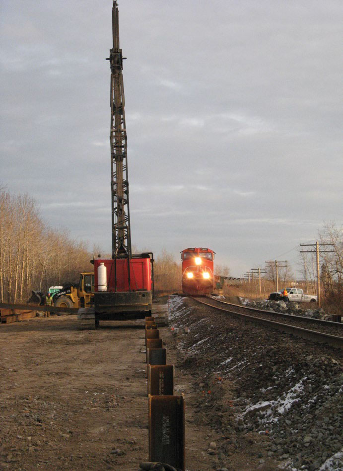 Driving piles beside railroad with train in background