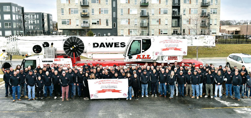 Dawes Rigging & Crane Rental team members gathered in front of machinery with banner for group photo.