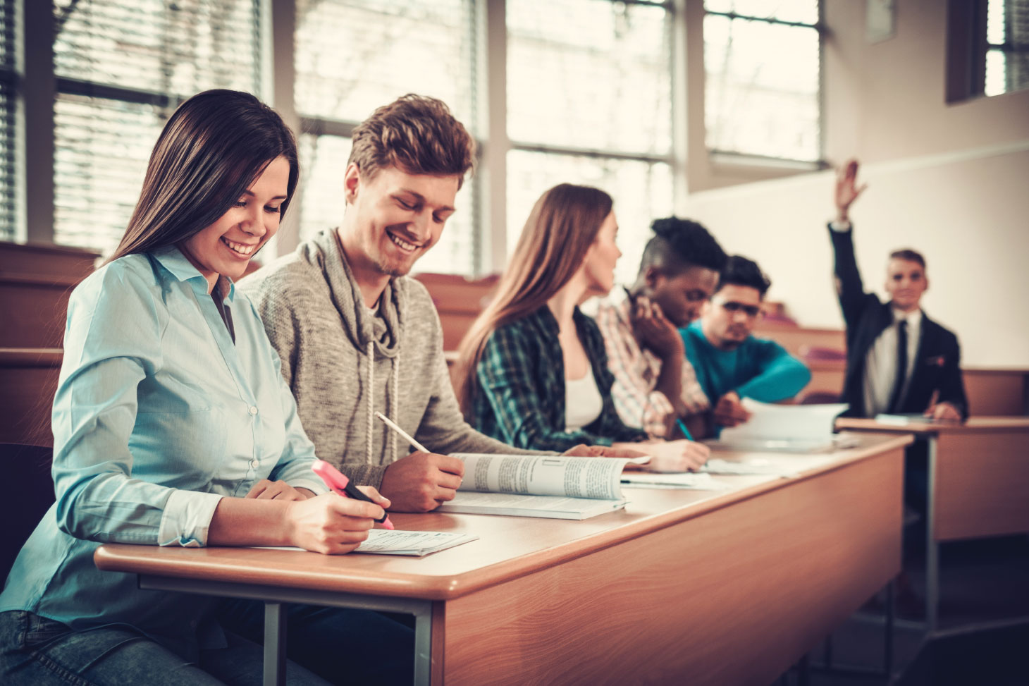 Students at desks with man in background raising hand