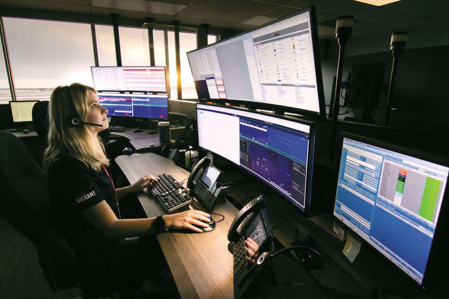 Woman with headset at desk monitoring many screens