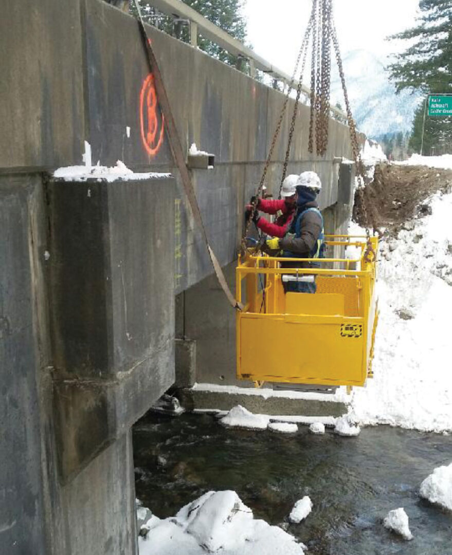 Workers scanning side of bridge above river