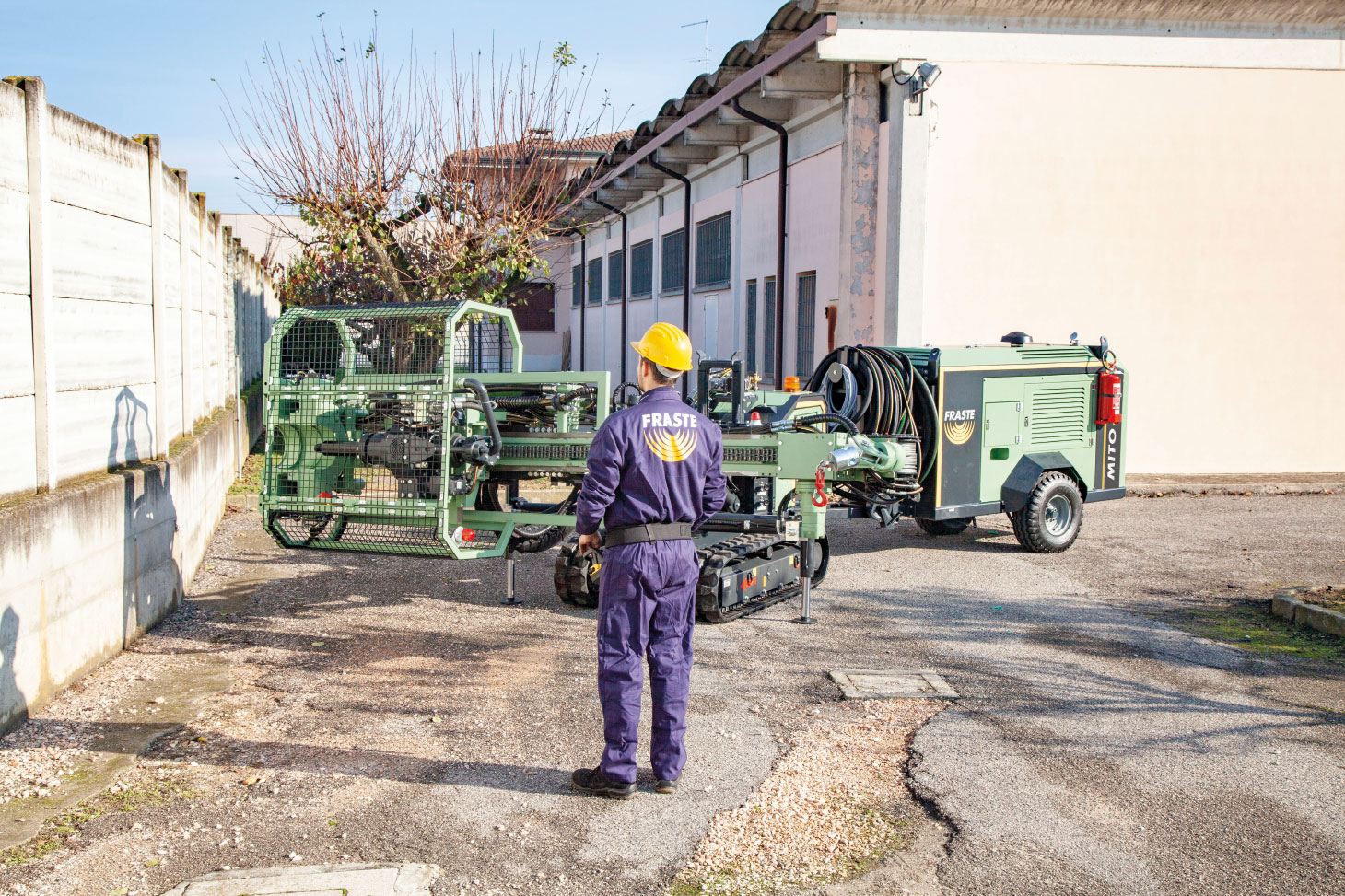 Employee in purple Fraste jumsuit and yellow helmet supervising work