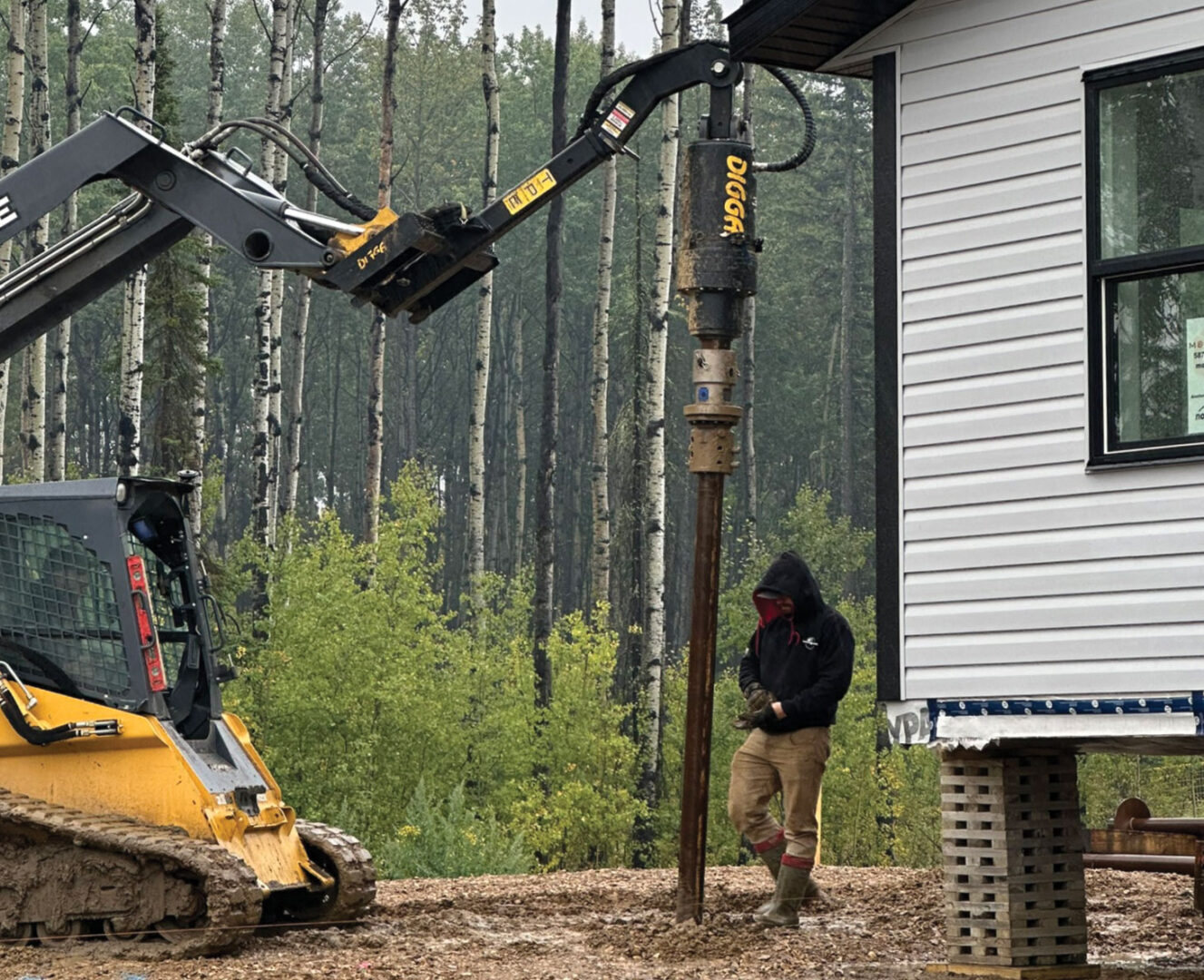 Auger installing pile with worker and house also in photo